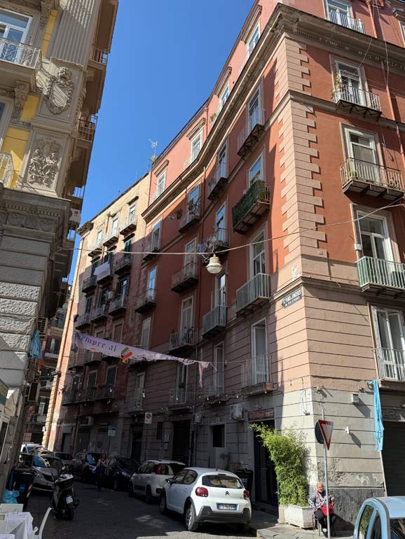 Admiring Naples architecture Building with red top and brown bottom. Cars parked on street.