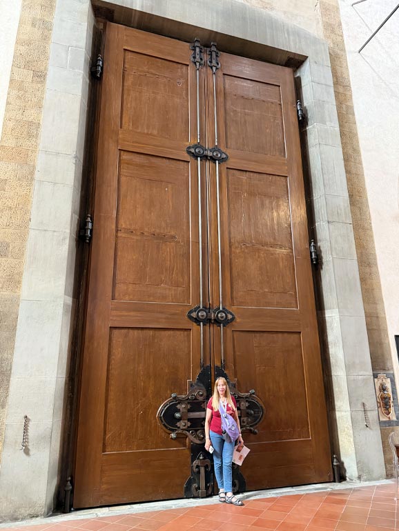 Anna standing next to brown door that is about 4 times her height.