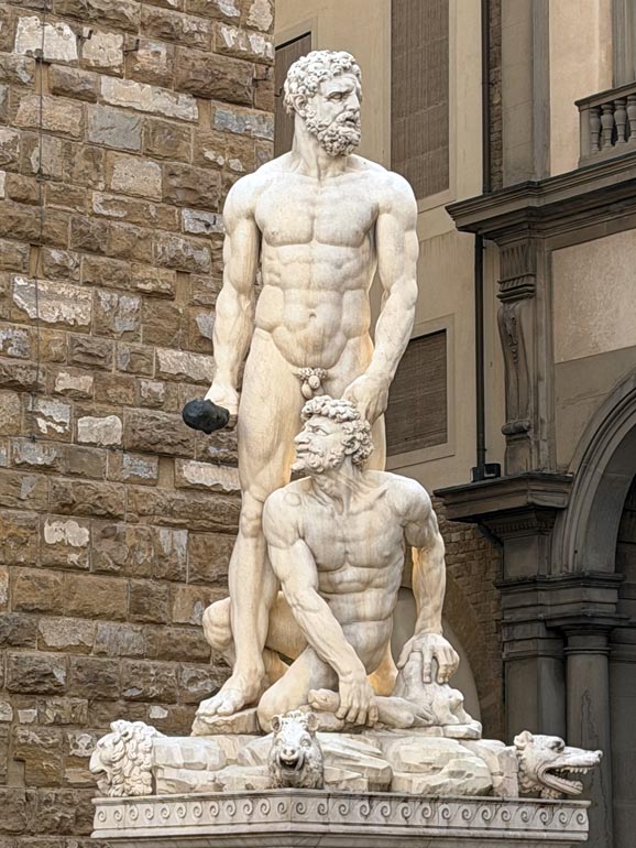 Two nude males figures. One standing and other is in front. Statue.