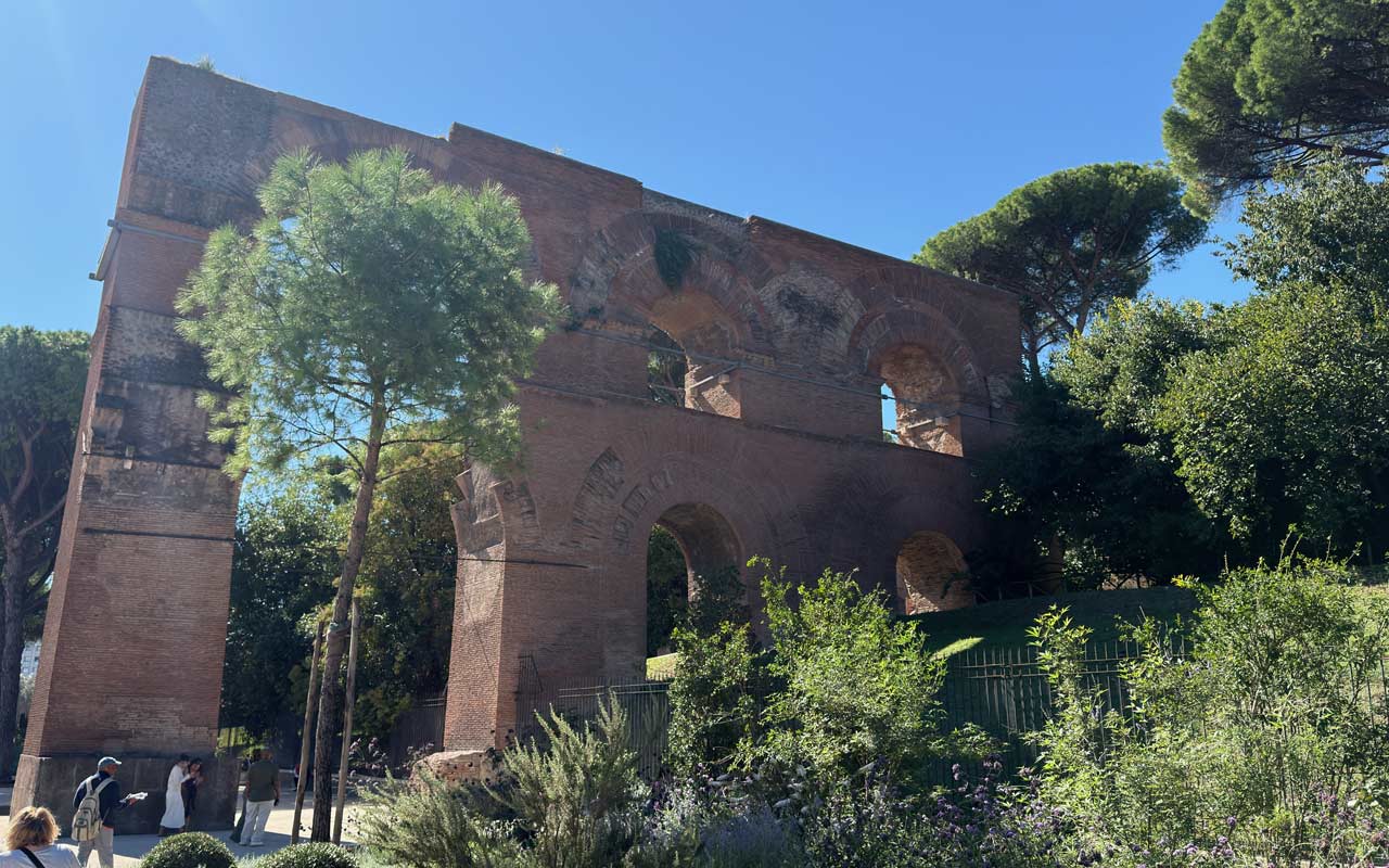 Nero Aqueduct by Palatine Hill with green trees around it. Ancient Roman Ruins.