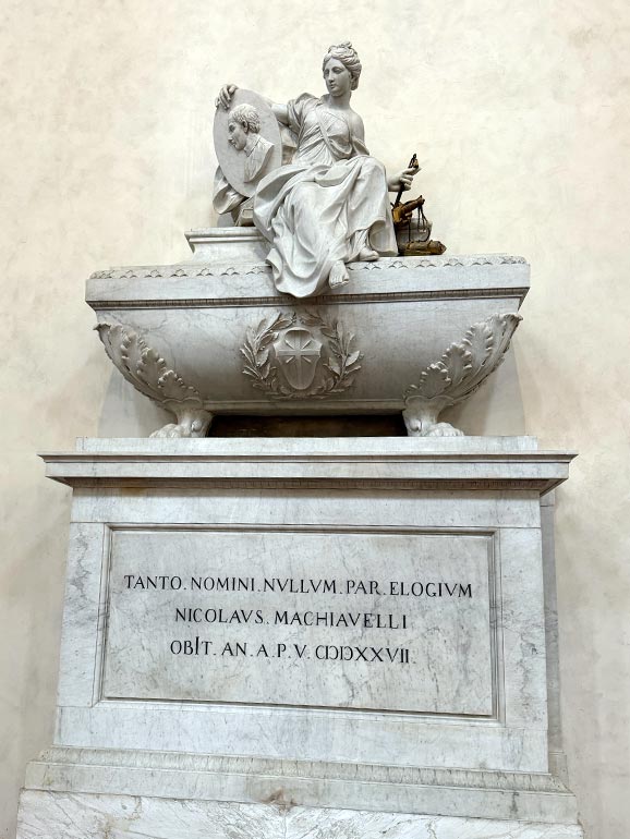 Woman with shield statue sitting on tomb. Gray in color.