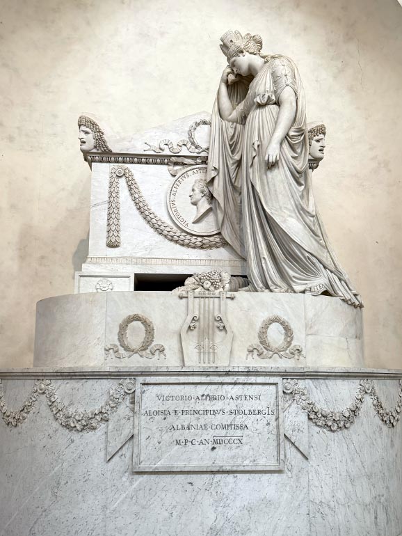 Woman in gown statue standing next to tomb.
