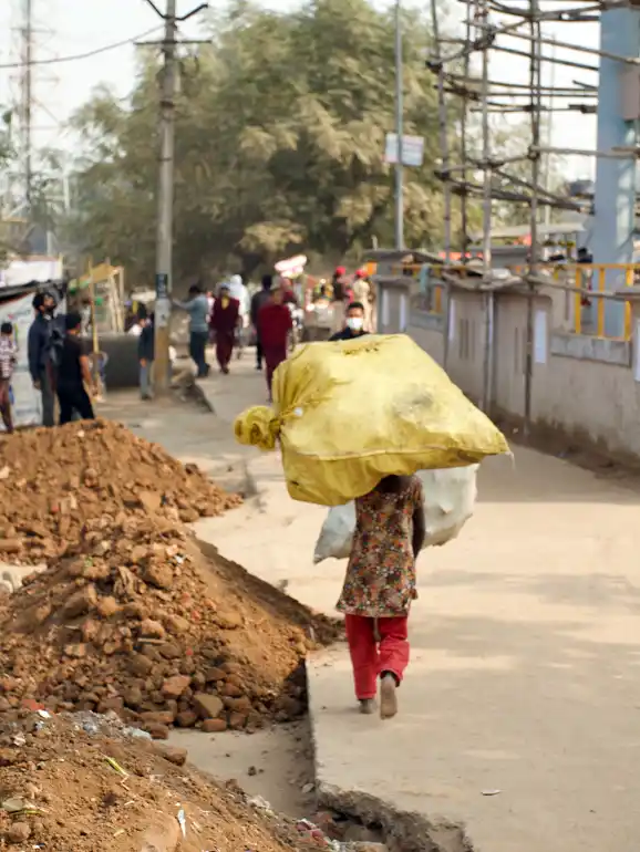 A person carries a large yellow bag of empty plastic bottles.