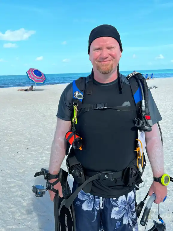 Gordon Eaton standing on beach in Scuba diving gear about to go into ocean.
